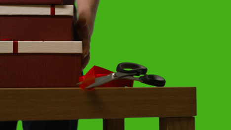 Close-Up-Of-Man-Picking-Up-Gift-Wrapped-Presents-In-Boxes-Decorated-With-Ribbon-On-Table-Shot-Against-Green-Screen-1